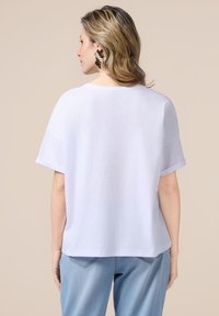 Camiseta blanca de manga corta con un ajuste relajado, textura suave, cuello redondo y dobladillo recto, combinada con jeans de color azul claro.