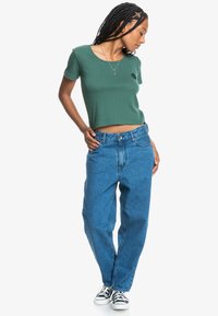 Zelený rib rovný crop top s okrúhlym výstrihom, skombinovaný s voľnými svetlomodrými džínsami z denimu a čierno-bielymi plátenými teniskami.