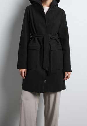 Schwarzer Kapuzenmantel mit taillierter Passform, ausgestattet mit zwei Vordertaschen und einem eleganten, strukturierten Design. Das Material wirkt weich und warm.