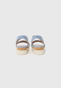 Sandales en suede bleu avec deux brides croisées, semelle en liège et fond en caoutchouc beige. Vue arrière montrant le design et la texture des brides.