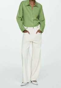 Camisa de botones de manga larga verde combinada con pantalones anchos blancos y zapatos de punta. Tejido texturizado y ajuste relajado.