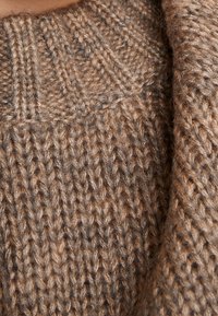 Ruskea neulottu neulepaita, jossa on teksturoitu, ribbineulospinta ja korkea kaulus. Kangas vaikuttaa paksulta ja pehmeältä, hieman pörröisellä pinnalla.