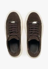 Brązowe zamszowe sneakersy z okrągłym noskiem, kontrastującą białą gumową podeszwą i ciemnymi sznurówkami. Posiadają teksturowaną cholewkę z akcentem w postaci logo na języku.