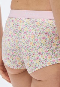 Medvilniniai šortai su gėlių raštu, rožinės spalvos elastiniu juosmeniu. Ant baltos fono matyti mažos rožinės ir geltonos gėlės.