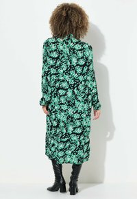 Vestito nero con motivo floreale verde, maniche lunghe, collo alto, dettaglio sulla schiena, abbinato a stivali neri fino al ginocchio, tessuto liscio.