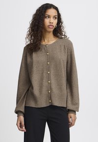 Ruskea neulecardigan, jossa on pyöreä pääntie, pitkät hihat ja napitettava etuosa, jossa on kultasävytettyjä nappeja. Pehmeä rakenne ja rento istuvuus.
