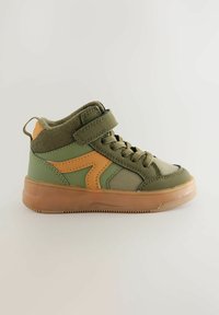 Sneaker montante verte avec des accents orange, présentant une tige en tissu texturé, une sangle ajustable et une semelle en caoutchouc pour la stabilité.