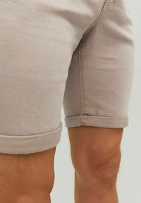Pantalones cortos de mezclilla beige con dobladillos enrollados, que presentan una textura suave y detalles de costura sutiles en las costuras laterales y el dobladillo.