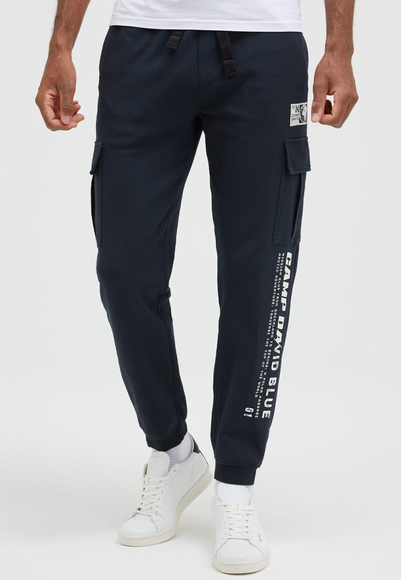 Marineblaue Cargo-Hosen aus Baumwollmischung mit Seitentaschen, elastischen Bündchen und Grafikdruck entlang des Beins.