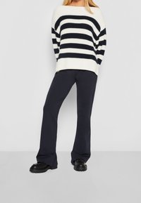 Maglione a righe in crema e navy; vestibilità ampia con spalle basse. Abbinato a pantaloni svasati scuri e scarpe nere con suola spessa.