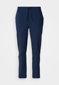Navyblauwe broek van een gestructureerde stof, met een elastische tailleband en trekkoord. Heeft taps toelopende benen met gestikte accenten bij de knieën.