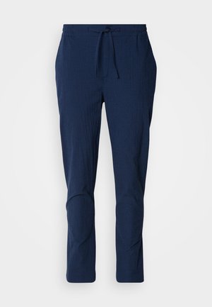 Navy blue pants with a textured fabric, elastic waistband, and drawstring. Features tapered legs with stitched accents at the knees.