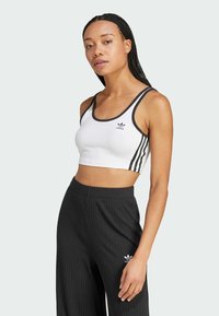 Witte cropped tanktop met zwarte afwerking en drie zwarte strepen aan de zijkant, gecombineerd met zwarte geribbelde brede broek met een logo.