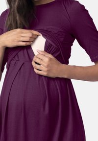 Lila gravidklänning med korta ärmar, med samlad tyg och en diskret öppning för amning. Mjukt, stretchigt material.