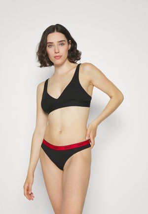 Svart bralette med brede stropper og dyp V-hals, sammen med svart truse med rød logo på midjen. Glatt tekstur og minimalistisk design.