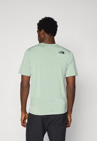 Camiseta de manga corta verde claro, hecha de una tela suave, con un logo negro en la parte superior de la espalda. Textura suave, escote redondo.