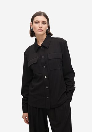 Chaqueta de camisa a rayas negras con dos bolsillos frontales, cierre de botones y un cuello clásico, hecha de una tela suave.