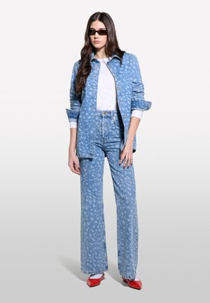 Jacket en denim bleu avec un motif subtil, T-shirt blanc et jeans bleu clair avec un design assorti. Associé à des chaussures rouges à talons pointus et des lunettes de soleil.