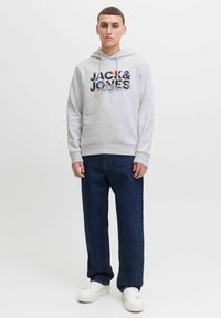 Sudadera gris con un logotipo multicolor en el frente, combinada con jeans de mezclilla azul oscuro y zapatillas blancas. Tejido suave, ajuste casual.