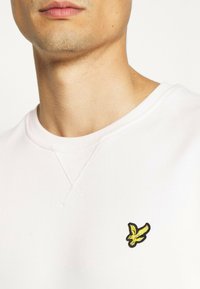 Felpa rosa chiaro con collo rotondo, caratterizzata da un piccolo logo ricamato di un uccello giallo e nero sul lato sinistro del petto.