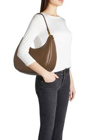 Borsa hobo in pelle marrone con una forma curva, texture liscia, tracolla regolabile e un sottile dettaglio dorato. Indossata a spalla.