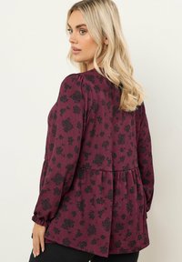 Blusa bordeaux con tessuto testurizzato, caratterizzata da un motivo floreale nero, maniche arricciate e un design peplum in vita.