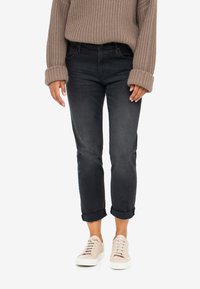 Mörkgrå jeans med uppvikt fåll, tillverkade av denim, matchade med ljusrosa sneakers. Tröjan är oversize med ett strukturerat stickat mönster.