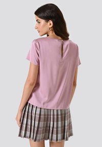 Kurzärmlige pinke Bluse mit einem Ausschnitt im Schlüsselanhänger-Stil und einem gefalteten karierten Rock in Grau, Burgunderrot und Schwarz, der eine weiche Textur aufweist.
