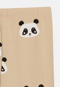 Leggings en tissu beige avec imprimés de visages de panda noirs et blancs ; texture douce ; taille élastique pour le confort et l'ajustement.
