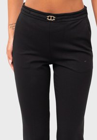 Zwarte broek gemaakt van een rekbare stof, met een platte tailleband met een gouden gesp detail en een gladde textuur.