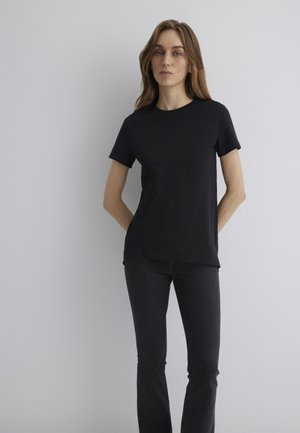 Schwarzes Baumwoll-T-Shirt mit Rundhalsausschnitt und kurzen Ärmeln, taillierte Passform, glatte Textur, kombiniert mit dunklen Jeans.