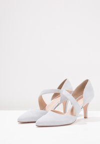 Grå mockastövlar med häl, spetsig tå, korsade remmar och en smal 5 cm klack, med en slätt inre och minimal detaljering.