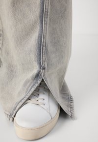 Lys blå denim vide bukser med sideskår, med kontrasterende syninger, parret med en hvid sneaker og beige sål.
