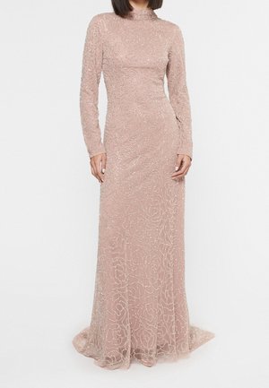Kobieta ubrana w długą do ziemi, z długim rękawem suknię w kolorze różowym z delikatnymi, spiralnymi wzorami z koralików i wysokim dekoltem.