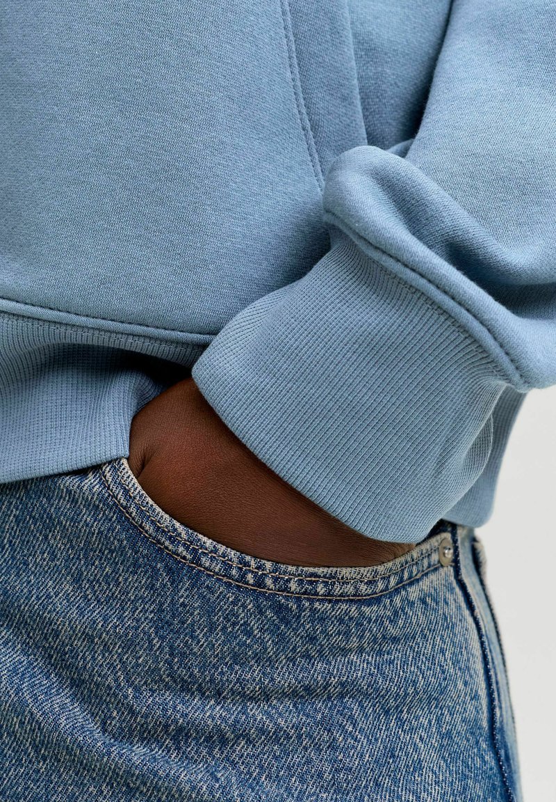 Hele sinine pusa soonikutega mansettidega, kombineeritud tumedate denimist teksadega, millel on sile tekstuur ja nähtavad õmblusetdetails.