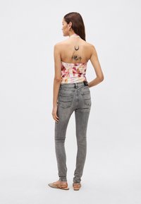 Top na ramiączkach z różowo-pomarańczowym wzorem tie-dye, zestawiony z szarymi obcisłymi jeansami. Widoczny tatuaż na plecach. Obuwie w jasnobrązowym kolorze.