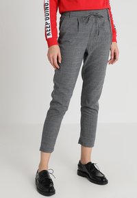 Grå rutiga byxor med dragsko i midjan, slim fit och avsmalnande ben, i kombination med svarta lackskor.