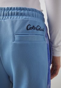 Light blue joggers with a textured finish. Features a back pocket and black "Carlo Colucci" logo on the waistband. Elastic waistband included.