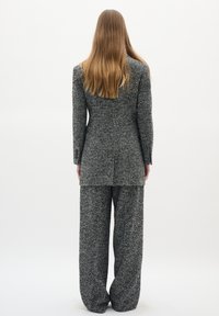 Pelēka houndstooth žakete ar atbilstošām platām biksēm, ar teksturētu audumu un pielāgotu siluetu, skatīta no aizmugures.