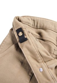 Beige cotton pants with ribbed texture. Features button closure and black fabric loop near top. Visible stitching and metallic buttons.