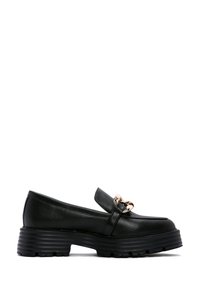 Mocassin en cuir noir avec semelle épaisse striée et détail de chaîne dorée sur le dessus, incliné pour montrer le côté extérieur de la chaussure.