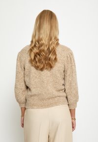 Bežani pulover teksture s napuhanim rukavima, s okruglim izrezom i rebrastim rubom. Lagano pleteni materijal prikazan s leđa.