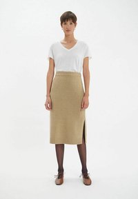 Jupe midi en maille beige avec fente latérale, ourlet côtelé et taille élastique, associée à un t-shirt blanc à col en V et des ballerines marron.