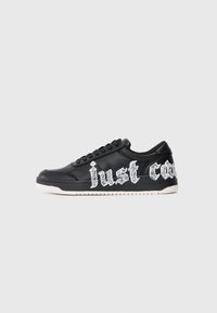 Mustad mustad sneaker, mille valge tallaga ja paeltega, mille peal on suured valged gooti stiilis tekstid, mis osaliselt ütlevad "just co".