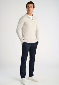 Jasno beżowy, długi rękaw polo z kołnierzykiem, zestawiony z granatowymi spodniami i białymi trampkami, charakteryzuje się dopasowanym krojem i gładką teksturą.