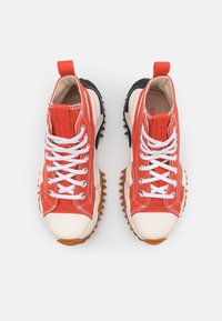 Sneakers in tela rossa con lacci bianchi, punta beige e suola nera robusta con punte appuntite. Sono presenti dettagli di cucitura a contrasto.
