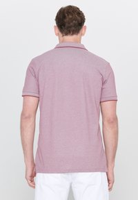 Polo à manches courtes en mauve clair avec col et poignets côtelés, présentant un bord contrastant sombre, fabriqué en coton mélangé doux et texturé.