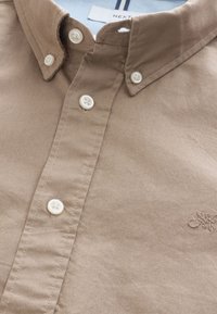 Lichtbruine gekorrelde shirt van katoen, met witte knopen en een subtiele geborduurde logo op de borst, zachte textuur.