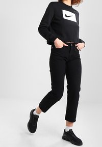 Sweatshirt noir court avec le logo Nike blanc, associé à un jean noir et des baskets noires. Possède des cordons de serrage ajustables à la taille.