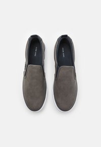 Chaussures à enfiler en cuir gris, avec une texture lisse, des accents élastiques sur les côtés et une semelle en caoutchouc blanc, arborant une étiquette de semelle intérieure sombre.